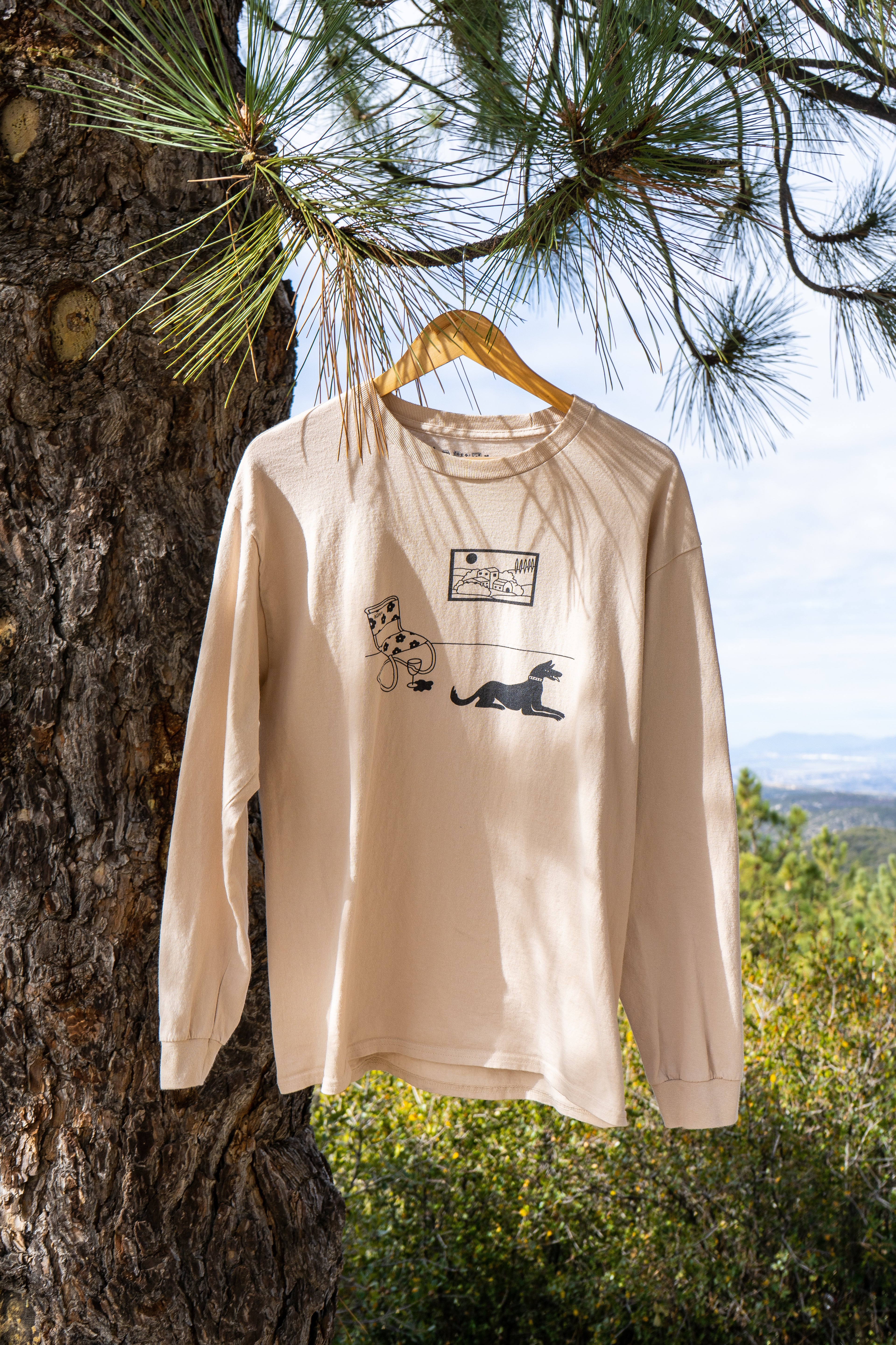 Beige long-sleeve shirt with graphic design hanging on a tree branch outdoors