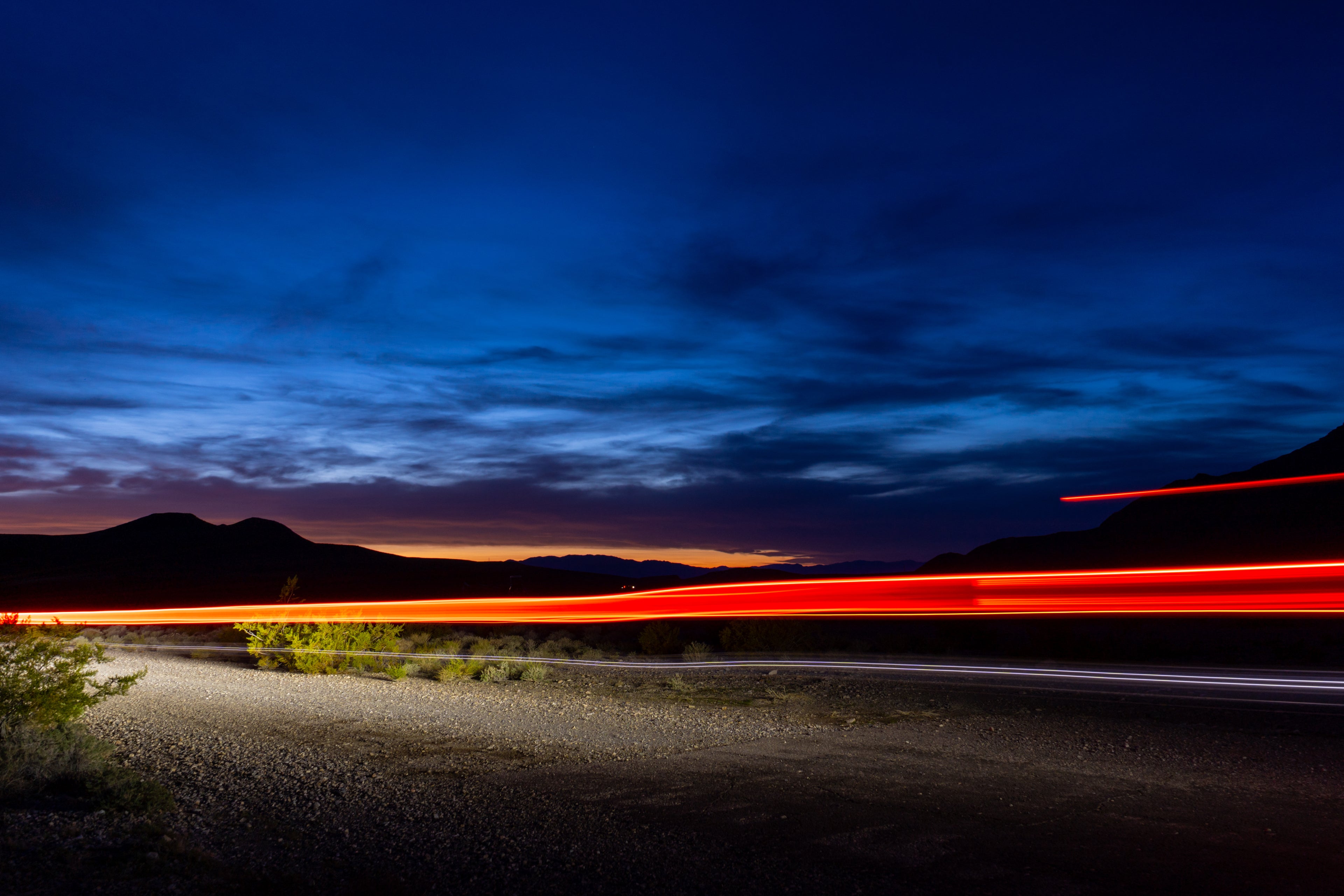 Long exposure of a road with vehicle lights at dusk or dawn, mountains in the background.
