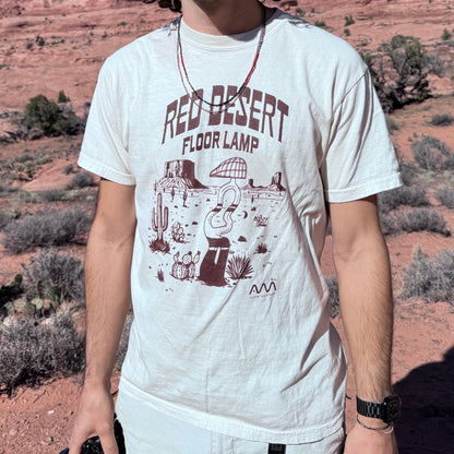 Man wearing sunglasses and a graphic t-shirt in a desert landscape with red rock formations.